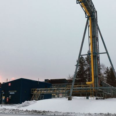 Putkisilta tien yli Outokummun Tornion tehtailla, taustalla palaa häkäkaasu poistoputken suulla.