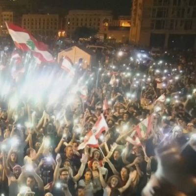 En dj blickar över publikhav under demonstrationerna i Beirut, Libanon. Publiken har flaggor i händerna och telefonernas ljus bildar ett ljushav bland publiken. 