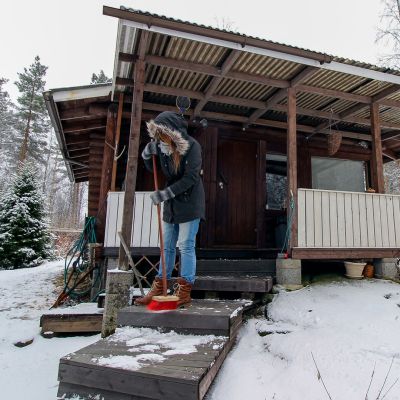 Nainen lakaisee mökin rappusia.