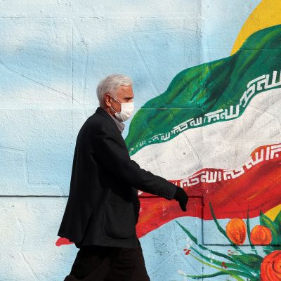 Mies kävelee Iranin lippua esittävän muraalin ohi.
