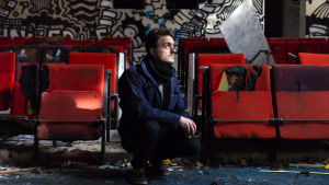 Viktor Granö har gjort poddserien "Framtidens människa" - klicka på bilden för att komma till seriens sida på Arenan Viktor Granö på huk i ett utrymme med röda bänkar och graffiti samt skrot på marken