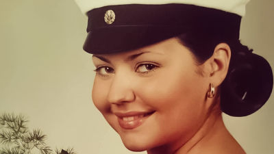 Daniela på sitt studentfoto. Hon har en knippe vita rosor i händerna, studentmössa och vänder sig snett och leende mot kameran.
