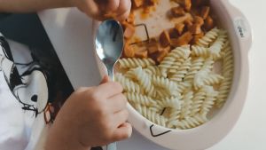 Många av Föräldrasnacks lyssnare hade tankar om vilken mat som skulle serveras för barnen. Många har ändå fått släppa på sina krav och tankar. Pasta och knackkorv serveras istället regelbundet hemma hos Rebecka också. En portion med pasta och knackorvssås. Ett barn håller i en sked ovanför portionen.