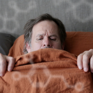 Patrik (Robin Svartström) makaa sängyssä raottaen peittoa ja katsoen alavartaloaan. 
