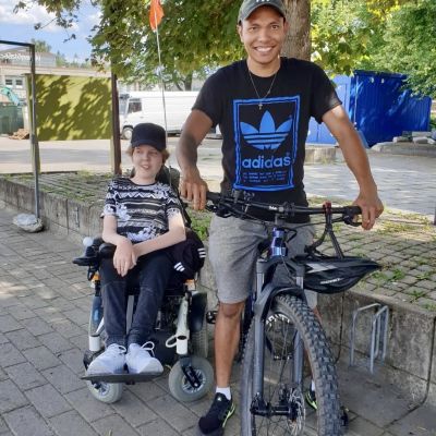 Poika pyörätuolissa ja nuori mies maastopyörän kanssa 