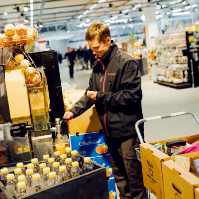 myyjä puristaa appelsiinimehua kaupassa