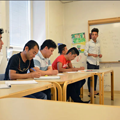 En ung invandrare lär ut finska till andra invandrare i ett klassrum.