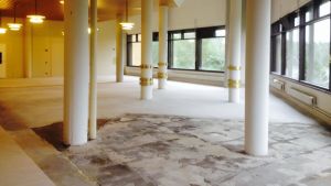 Institutet renoveras som bäst för den framtida semesterbyns behov. En hall med vita pelare och golv som renoveras. Ljus strömmar in genom fönstren.