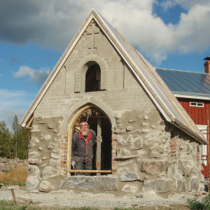 Mies kurkistaa pienen, rakenteilla olevan kirkon oviaukosta.