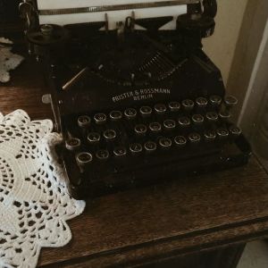 I dark academia framhävs det analoga - och det är inte ovanligt att användare på TikTok och Instagram ses skriva på skrivmaskin eller med fjäderpenna och bläck. En gammaldags skrivmaskin på en mörk byrå med en vit bordsduk bredvid.
