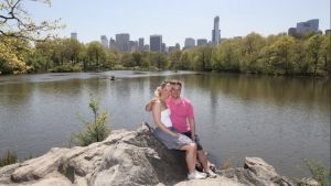 Christer och hans nuvarande fru Tuula på bröllopsresa i New York. “Två dagar av resan satt jag på hotellrummet och drack sprit rakt ur flaskan. Romantiskt.” Christer Schoultz med fru på bröllopsresa poserar vid sjö med stadsvy i bakgrunden.