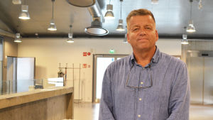 Per Högström. En medelålders man i kragskjorta står inne i Borgå Konstfabrik. Bakom honom syns taklampor och grå väggar.