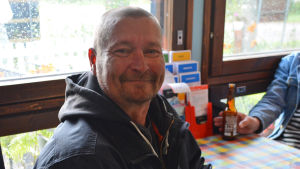 Pete Tupola undrar hur ägarbytet påverkar företagarna i området. En man sitter vid ett bord. Han ler mot kameran och håller i en ölflaska.