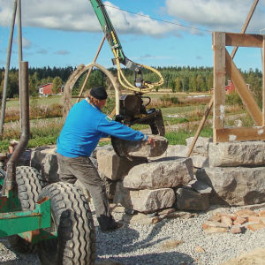 Kaksi miestä rakentamassa kirkkoa työkoneen avustamana.