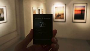 Ahmed fick sina foton uställda på Galleri Zebra i Karis. Ahmed had his own exhibition at Galleri Zebra in Karis. En hand som håller ett svart visitkort, i bakgrunden fotografier på en vit vägg.