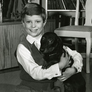 Kungen som ung kronprins. Svartvit bild av Kung Carl XVI Gustaf som barn, i famnen håller han en hund.
