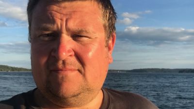 Närbild på en medelålders man. I bakgrunden syns havet.