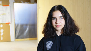 Michelle Sarström ser framemot att få egna klassrum En flicka klädd i svart munkjacka står inne i ett halvfärdigt hus. Hon tittar in i kameran.