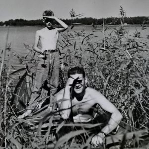 Mustavalkoisessa kuvassa 1950-luvulta nuori poika ja mies kaislikossa ilman paitaa