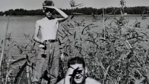 Mustavalkoisessa kuvassa 1950-luvulta nuori poika ja mies kaislikossa ilman paitaa
