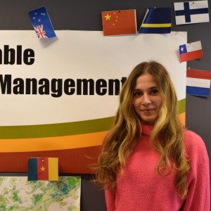 En ung kvinna framför en poster där det står Sustainable Coastal Management. Runt postern finns det flaggor från flera olika länder.