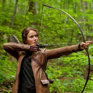 Närbild på Katniss Everdeen (Jennifer Lawrence) som spänner sin båge i skogen. 