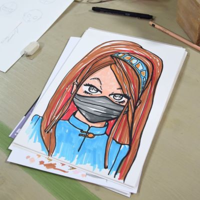 Ett pappersark med ett tecknat kvinnoporträtt. Kvinnofiguren är en ninja tecknad i mangastil. Ninjan har en svart ansiktsmask, långt brunt hår och en blå jacka.