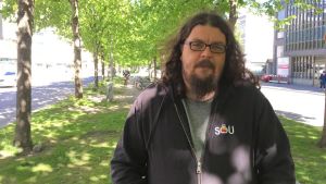 Jonas Rönnqvist. En porträttbild av Jonas Rönnqvist som står i mitten av en esplanad. Han bär en svart munkjacka och glasögon.