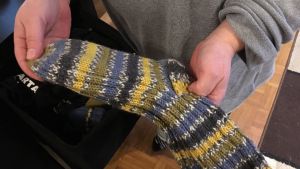 En okänd person donerade yllesockor för barnen i familjen. Mamman känner sig rörd av den hjälp som främmande människor erbjuder. Händer håller i en yllesocka.