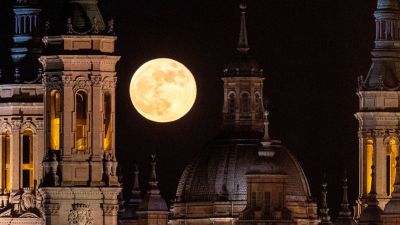 En citrongul enorm måne syns ovanför tinnar och torn mot en svart himmel.