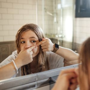 en tonårig flicka klämmer en finne framför spegeln