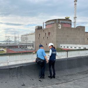 Kaksi IAEA:n tarkastajaa seisoo ydinvoimalan edessä.
