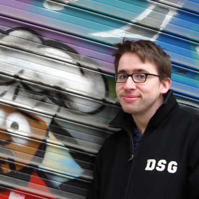 fredrik strage står leende mot en plåtvägg med en graffittimålning av karaktären chef från serien south park. 