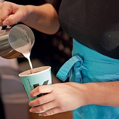 Kahvilatyöntekijä kaataa maitoa kahviin