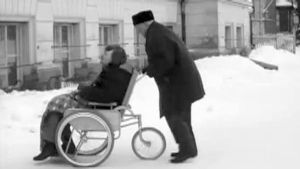 Vanha mies työntää nuorempaa pyörätuolissa