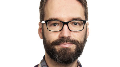 Man med skäg och glasögon mot vit bakgrund.