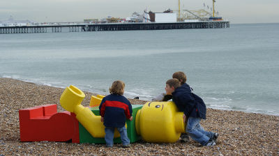 Barn hänger på en stor legogubbe på en strand
