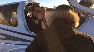 De professionella piloterna Nikke Rahkonen och Tomi Jääskeläinen gjorde sin första visit på Pyttis flygfält som en mellanlandning under rutten från Malm i Helsingfors till Uttis i Kouvola. Flygkapten Esa Korjula som ansvarar för verksamheten på flygfältet i Pyttis gick för att hälsa på dem. Två män sitter inne i styrhytten på ett litet flygplan. Framför dem står någon klädd i en svart rock med ryggen vänd mot kameran.