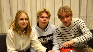 Elida, Jonathan och Frank ska undervisa åttor i första hjälpen nästa år. De tre ungdomarna sitter på en soffa och kollar i ryggsäcken på bordet framför.