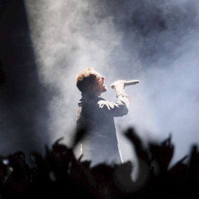 Bono som är sångare i U2 sjunger omgiven av fans på en rökig scen.