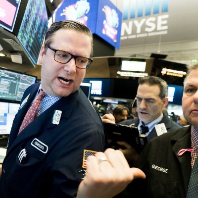 New Yorkin pörssi toiminnassa 9. helmikuuta 2018. Keskellä mies kommentoi jotain taaksepäin, ympärillä on muita miehiä, yksi on puhelimessa, toinen näppäilee tablettitietokonetta, kolmas katselee ilmeisesti monitoreita.