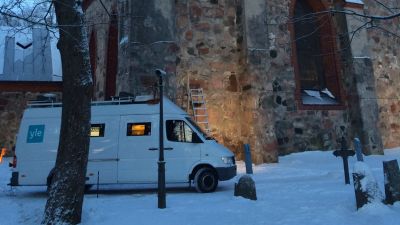 Yles vita sändningsbil står utanför en kyrka. Det är snö på marken.