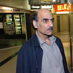 En man med buskiga ögonbryn och mustasch står bredvid en reklampelare med den franska filmaffischen för Steven Spielbergs film The Terminal.