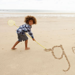 Liten flicka skriver g eller g på två olik sätt i sanden med en pinne