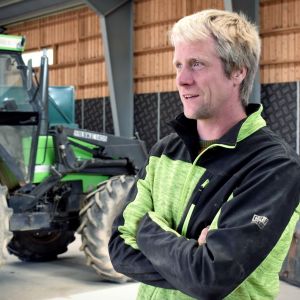 Claus Blomberg står i en lagerhall framför en grön traktor.
