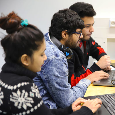 Tre studerande från Indien och Nepal, Elisha Baniya, Dhruv Verna och Vinayak Chaturvedi, sitter framför sina datorer och studerar.
