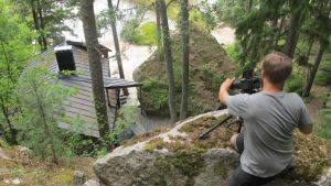 Fotograf Mikko tar bilder med annorlunda bildvinklar. Fotografen Mikko tar bilder på en stugan uppifrån ett berg