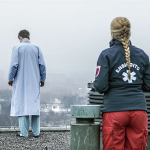 Sairaalasarjan ensihoidon työntekijä seuraa katon reunalla seisovaa potilasta.