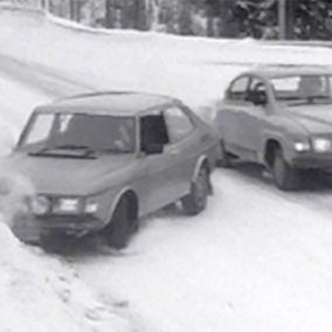 Mustavalkoisessa kuvassa kaksi Saab-merkkistä autoa on törmätä lumisella tiellä.
