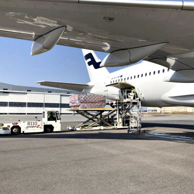 Bild på vitt Finnair-flygplan. På bilden lastas materiel ut ur planet. 